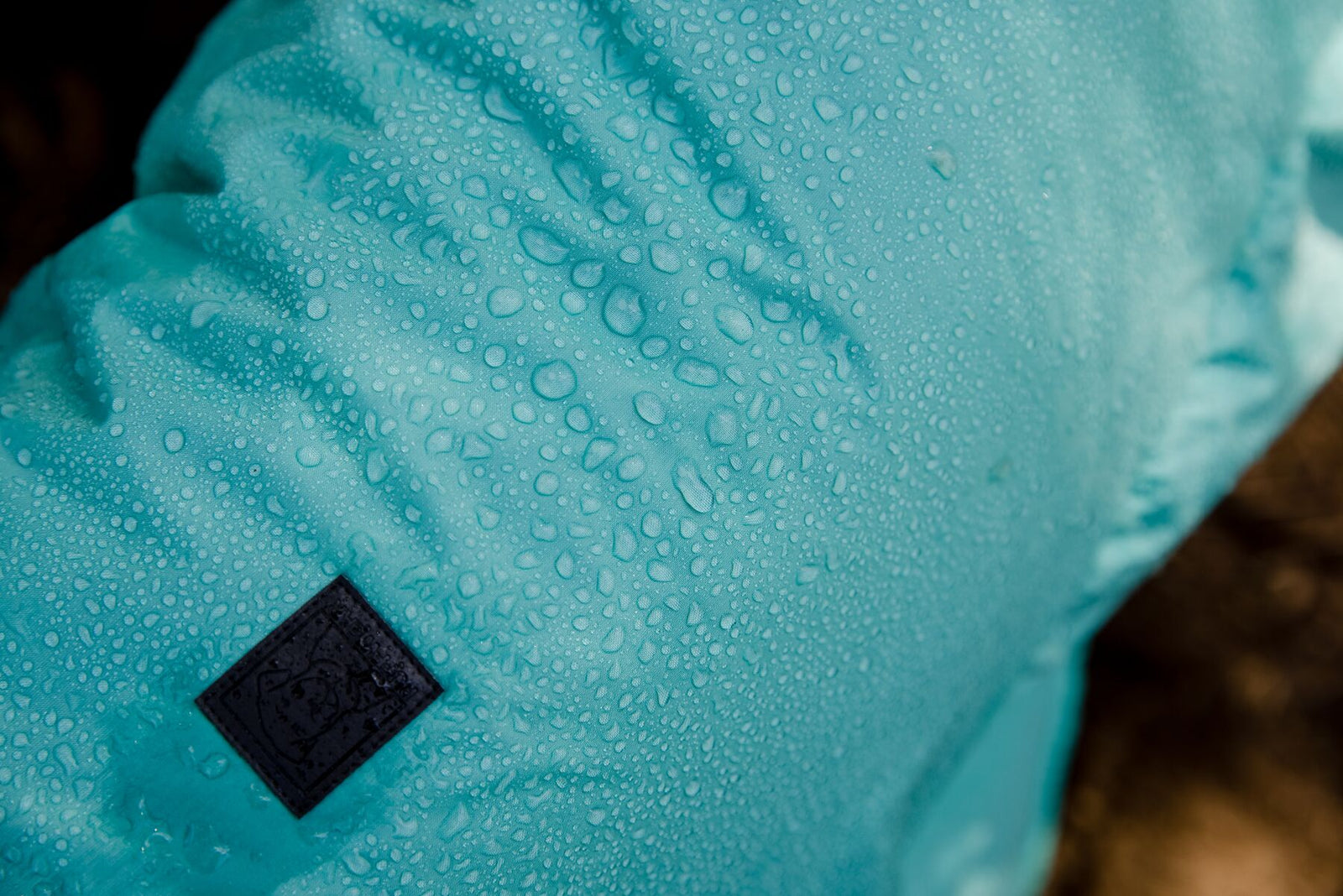 Close-up of the Aurora Teal waterproof shell of the Ruffwear Dirtbag™ Dog Towel beading water droplets on a dog's back, with the Ruffwear woven label visible, demonstrating the DWR waterproof coating in action