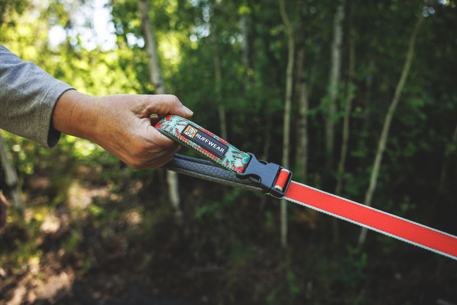 Ruffwear Crag Reflective Lead in Tropical Bloom - close-up of padded handle held in hand on a woodland trail, showing Ruffwear branding and floral Tubelok webbing