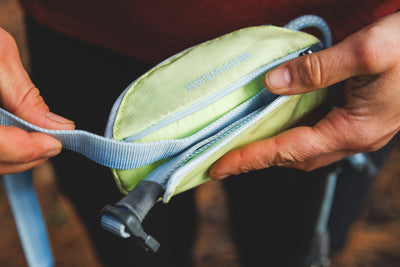 Close-up of hands holding the Sunny Lime stow bag showing the adjustable strap and side-release buckle on the Ruffwear Hitch Hiker Dog Lead