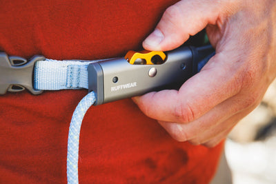 Close-up of a hand pressing the thumb button on the Ruffwear HitchLock rope adjuster showing the yellow button and Ruffwear branding