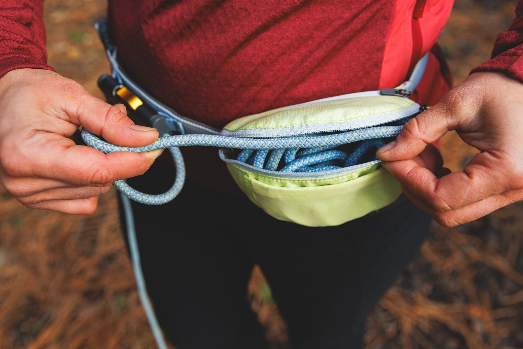 Hands pulling the kernmantle rope from the open stow bag on the Ruffwear Hitch Hiker Dog Lead in Sunny Lime worn as a waist belt