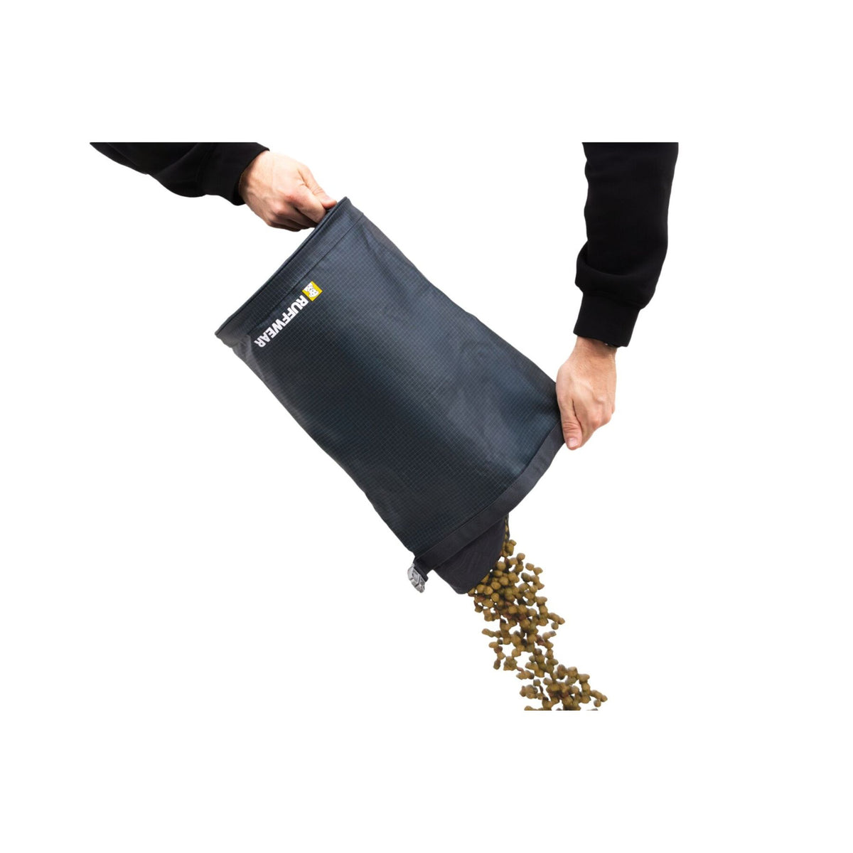Hands tipping the Ruffwear Kibble Kaddie dog food carrier in Basalt Gray upside down on a white background, pouring kibble from the fold-out spout at the base