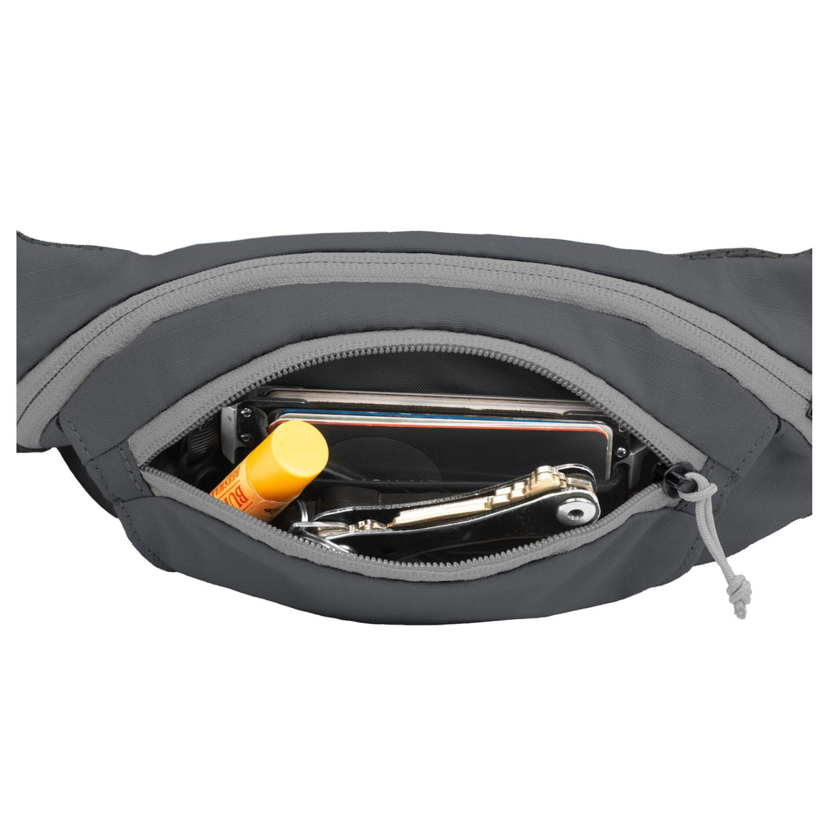Ruffwear Home Trail hip pack in Granite Gray open on a white background, showing the main zippered compartment containing a smartphone, multi-tool, and lip balm, with the water-resistant zip and grey pull tab visible
