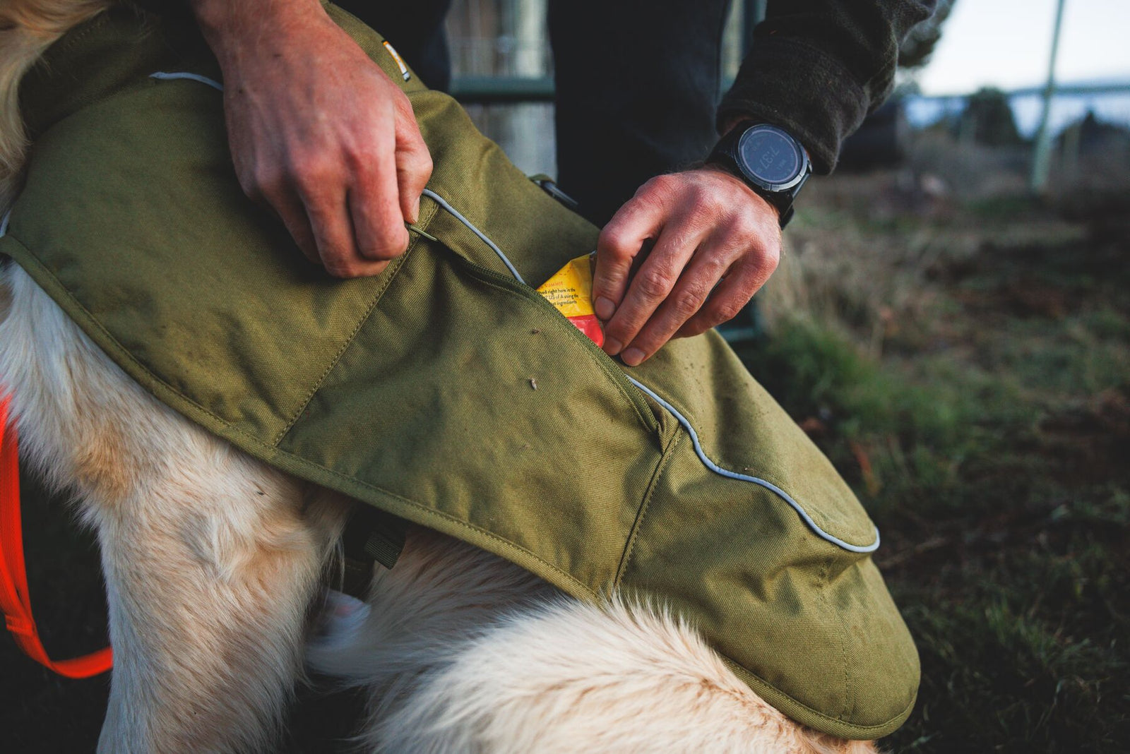 Close-up of owner accessing zippered pocket on Ruffwear Overcoat Fuse insulated dog vest in Cedar Green - low-profile storage pocket for walk essentials